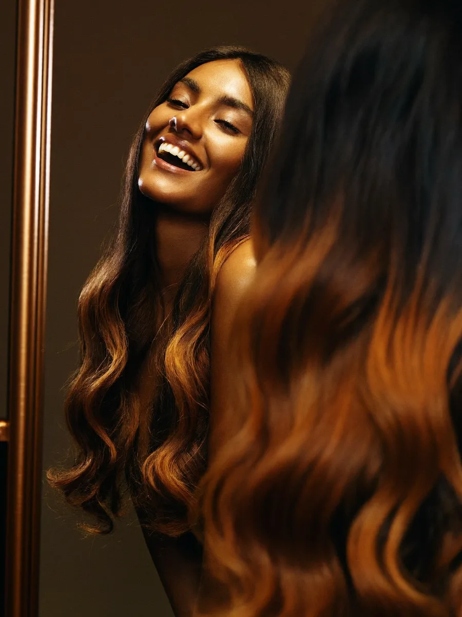 An Indian woman admiring her luminous caramel balayage in the salon mirror